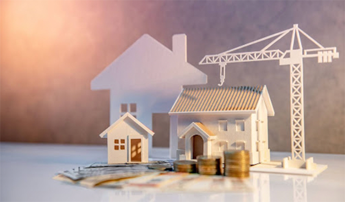 Paper house model and money stack with crane in background.